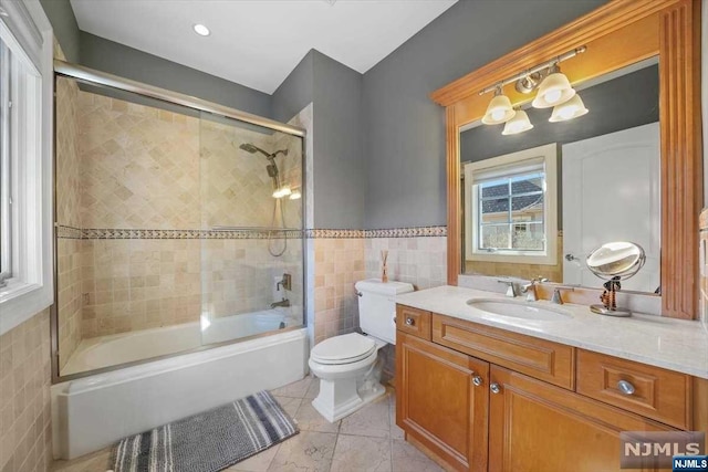 full bathroom featuring vanity, toilet, bath / shower combo with glass door, and tile walls