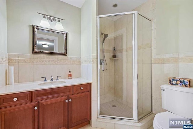 bathroom with vanity, toilet, a shower with shower door, and tile walls