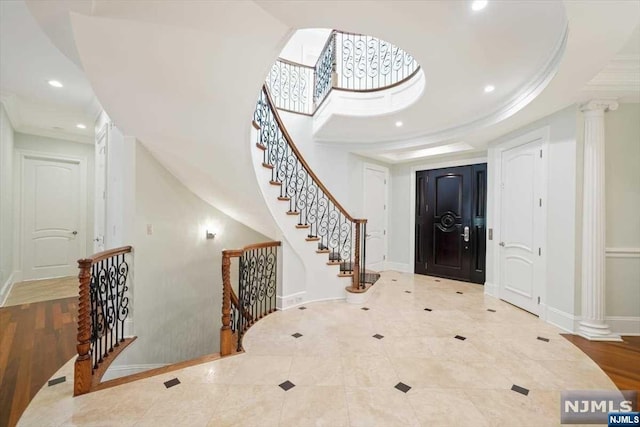 entrance foyer featuring a tray ceiling, ornate columns, and light hardwood / wood-style floors