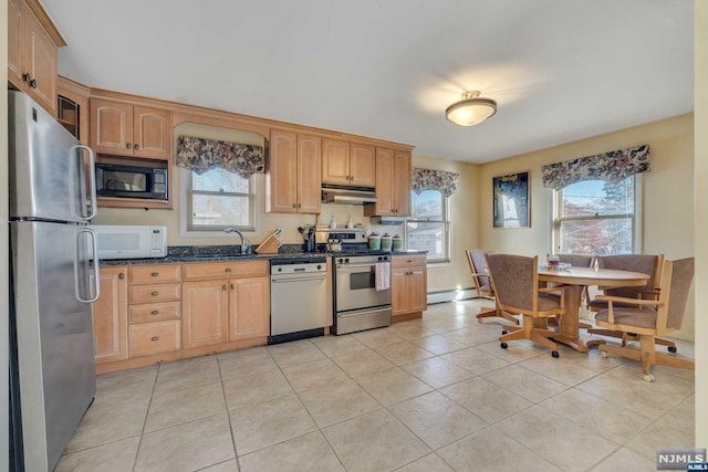 kitchen with light tile patterned floors, appliances with stainless steel finishes, baseboard heating, dark stone counters, and sink