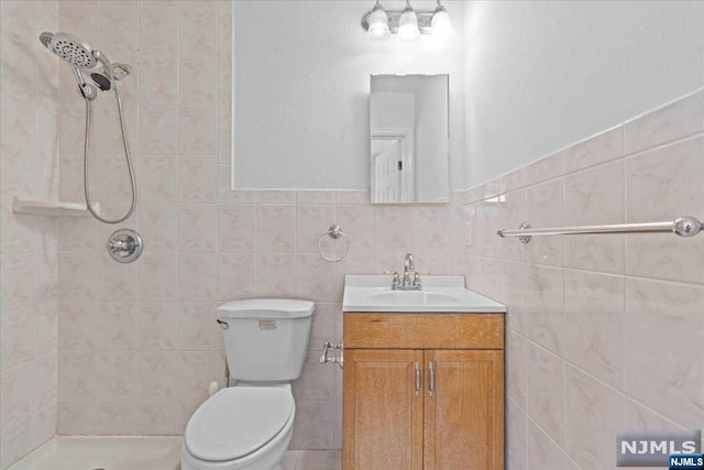 bathroom featuring vanity, toilet, tile walls, and a tile shower