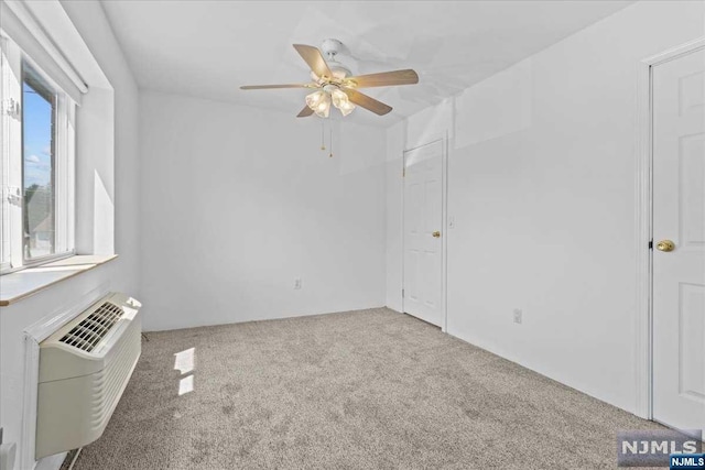 carpeted spare room with a wall unit AC and ceiling fan