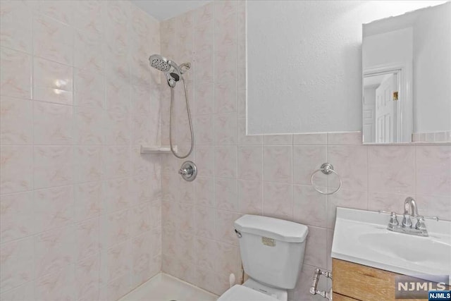 bathroom featuring tiled shower, vanity, tile walls, and toilet