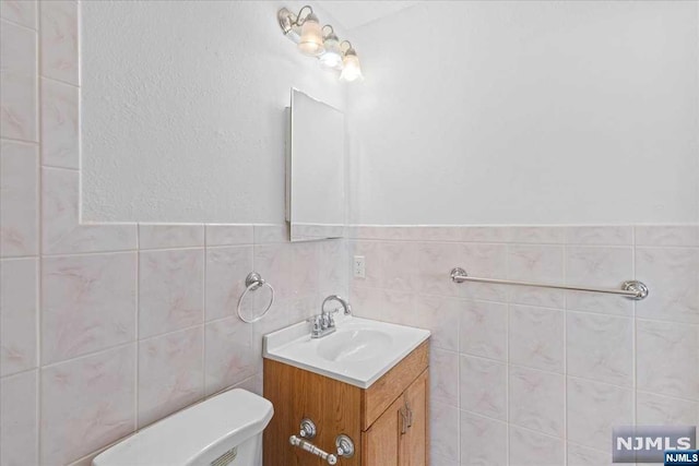 bathroom with vanity, toilet, and tile walls