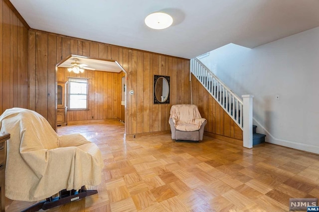 living area featuring ceiling fan, wood walls, and light parquet floors