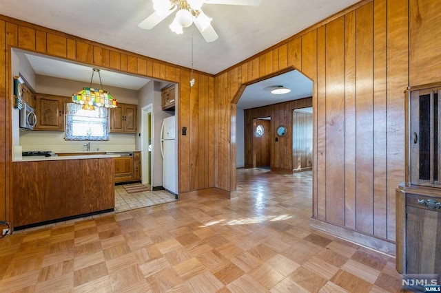 kitchen with light parquet floors, white refrigerator, hanging light fixtures, wooden walls, and ceiling fan