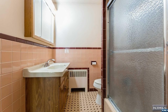 full bathroom featuring vanity, shower / bath combination with glass door, toilet, tile walls, and radiator heating unit