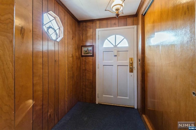 doorway to outside with carpet flooring and wood walls