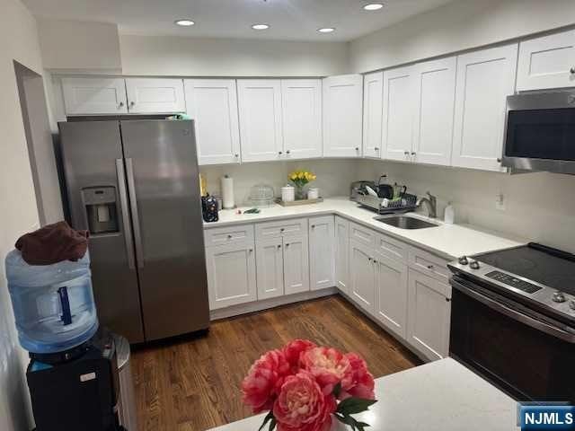 kitchen with white cabinets, appliances with stainless steel finishes, dark hardwood / wood-style flooring, and sink