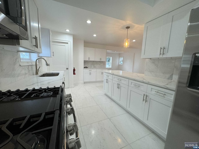 kitchen with appliances with stainless steel finishes, light stone counters, sink, white cabinets, and hanging light fixtures