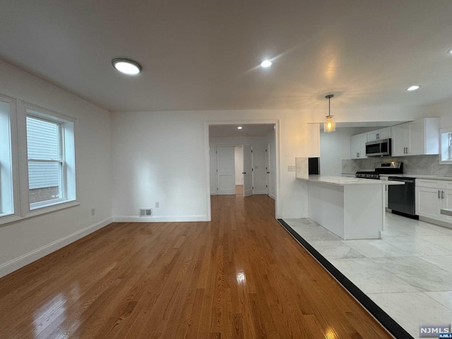 kitchen with appliances with stainless steel finishes, light wood-type flooring, backsplash, white cabinetry, and hanging light fixtures