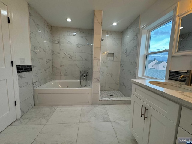 bathroom featuring plus walk in shower, vanity, and tile walls