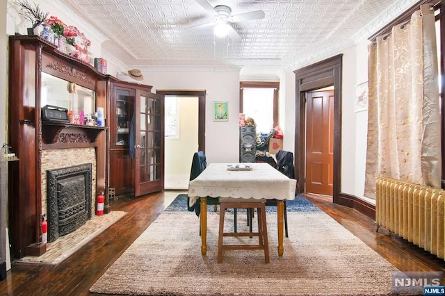 dining space with dark wood-type flooring, radiator, crown molding, ceiling fan, and a fireplace