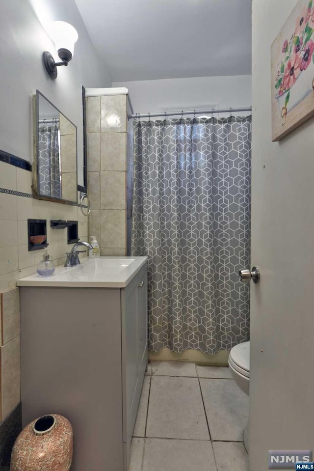 bathroom with a shower with curtain, tile patterned flooring, toilet, vanity, and tile walls