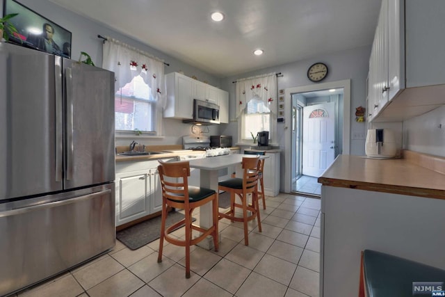 kitchen featuring white cabinets, appliances with stainless steel finishes, light tile patterned floors, and a healthy amount of sunlight