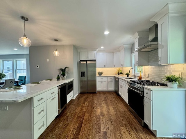 kitchen with white cabinets, wall chimney range hood, hanging light fixtures, appliances with stainless steel finishes, and dark hardwood / wood-style flooring