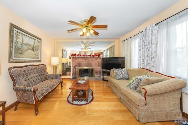 living room featuring ceiling fan, a fireplace, and light hardwood / wood-style floors