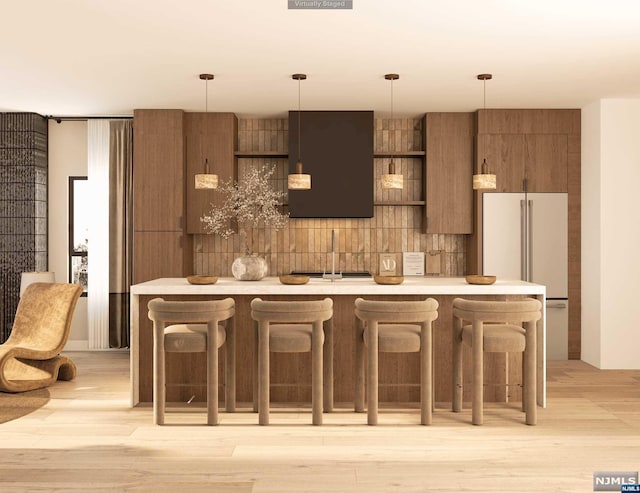 kitchen with high end white fridge, light wood-type flooring, tasteful backsplash, decorative light fixtures, and a kitchen bar