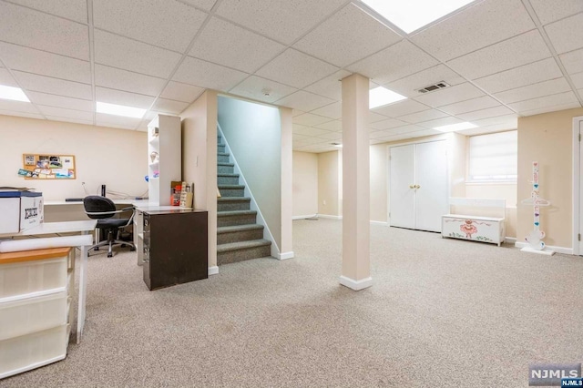 finished below grade area featuring visible vents, a drop ceiling, carpet flooring, baseboards, and stairs