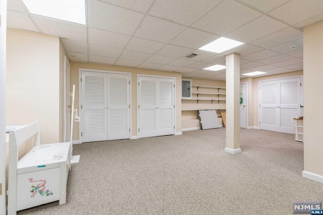 below grade area with visible vents, electric panel, a drop ceiling, carpet, and baseboards