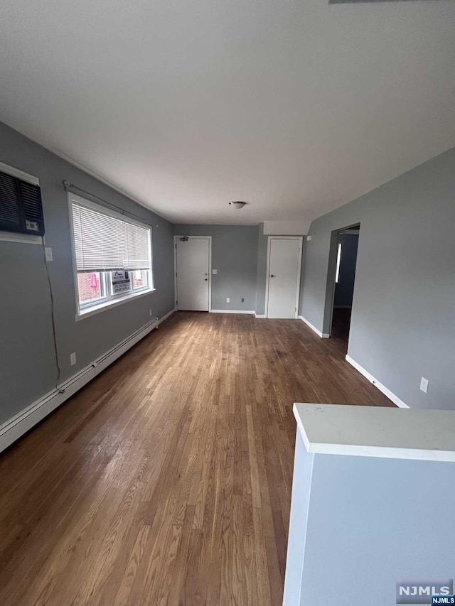 unfurnished living room with a wall mounted AC, a baseboard radiator, and hardwood / wood-style flooring