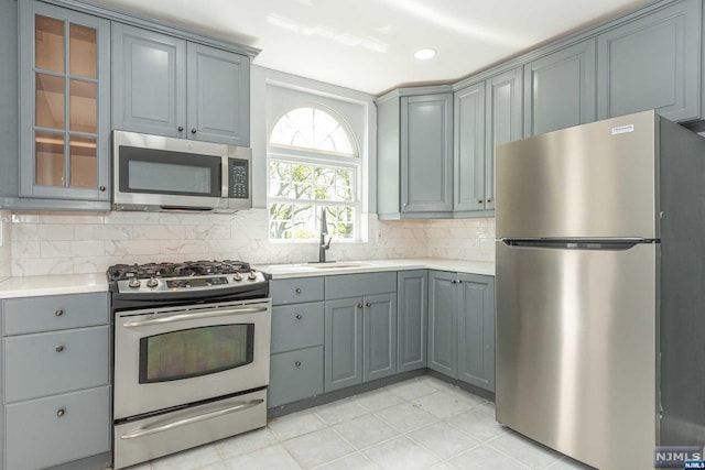 kitchen with tasteful backsplash, stainless steel appliances, sink, gray cabinets, and light tile patterned flooring