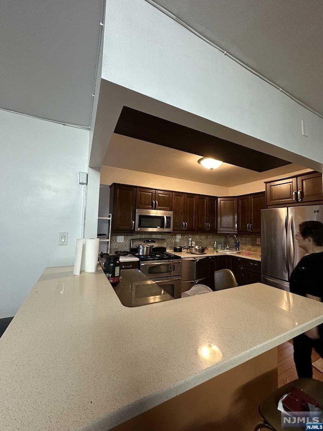 kitchen with dark brown cabinetry, a kitchen breakfast bar, tasteful backsplash, kitchen peninsula, and appliances with stainless steel finishes