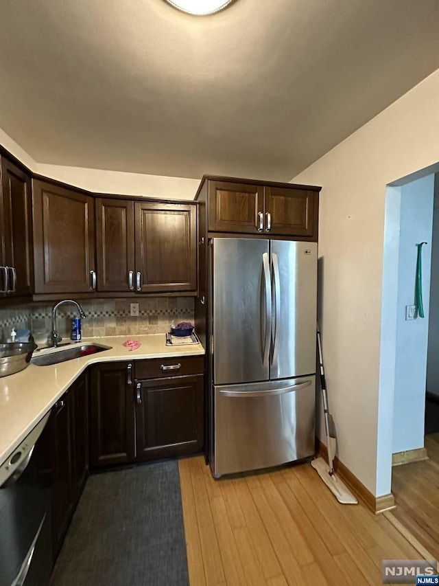 kitchen with dishwasher, sink, light hardwood / wood-style flooring, stainless steel fridge, and tasteful backsplash