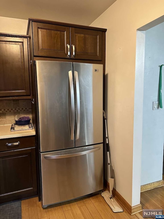 kitchen with dark brown cabinets, stainless steel fridge, light wood-type flooring, and tasteful backsplash