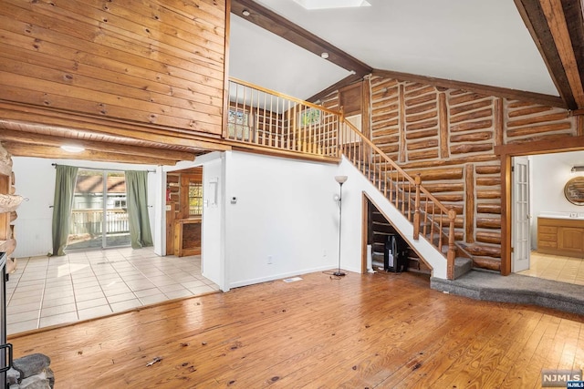 unfurnished living room with hardwood / wood-style floors, beam ceiling, high vaulted ceiling, and log walls