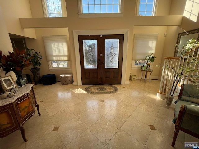 tiled entrance foyer with a healthy amount of sunlight, a towering ceiling, and french doors