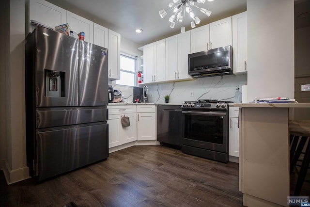 kitchen with appliances with stainless steel finishes, dark wood-type flooring, white cabinets, a chandelier, and a breakfast bar area