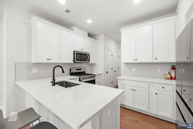 kitchen with white cabinets, kitchen peninsula, sink, and appliances with stainless steel finishes