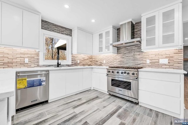 kitchen with decorative backsplash, white cabinetry, wall chimney exhaust hood, and stainless steel appliances