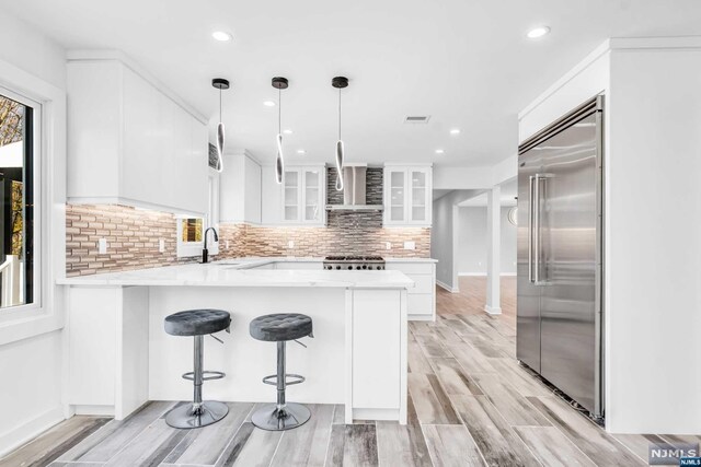 kitchen with white cabinets, hanging light fixtures, light hardwood / wood-style flooring, kitchen peninsula, and stainless steel appliances