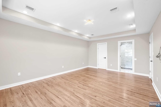 spare room featuring a tray ceiling and light hardwood / wood-style flooring