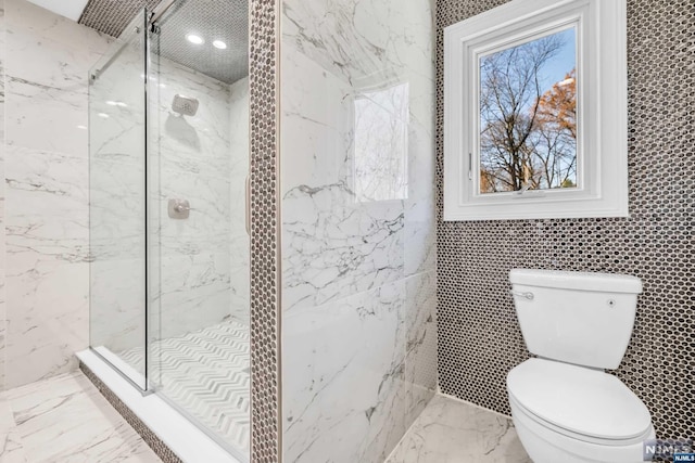 bathroom with toilet, tiled shower, and tile walls