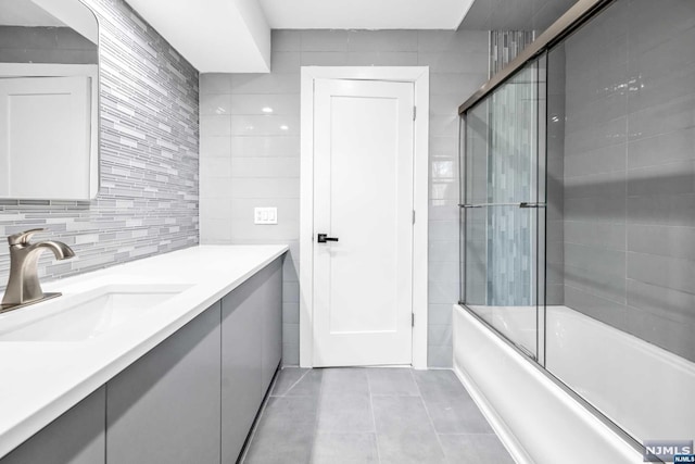 bathroom featuring tile patterned flooring, vanity, bath / shower combo with glass door, and tile walls