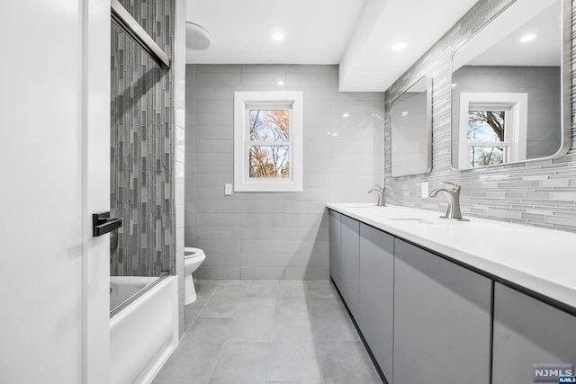 full bathroom with combined bath / shower with glass door, toilet, and tile walls