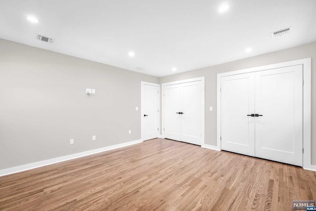 unfurnished bedroom featuring multiple closets and light wood-type flooring