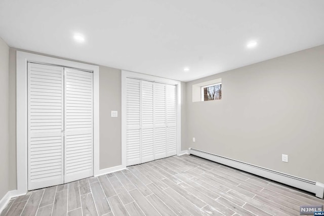 unfurnished bedroom featuring light hardwood / wood-style flooring, two closets, and a baseboard heating unit