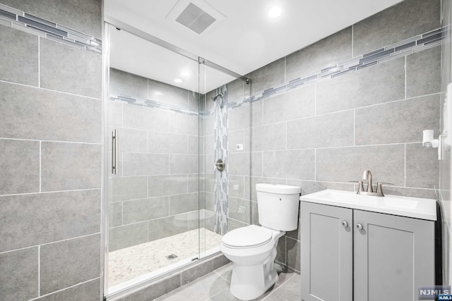 bathroom with vanity, tile patterned floors, toilet, tile walls, and a shower with shower door