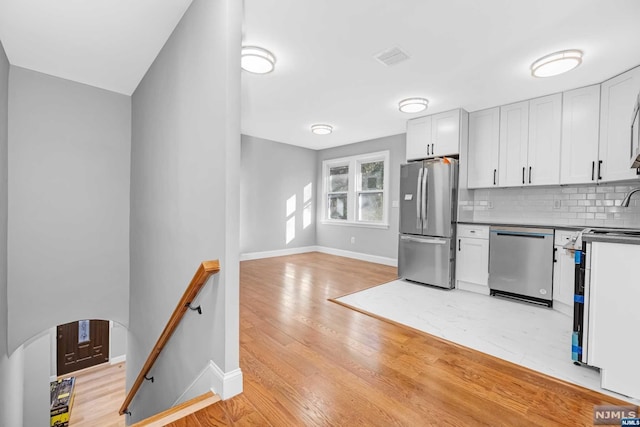 kitchen featuring white cabinets, decorative backsplash, light wood-type flooring, and appliances with stainless steel finishes