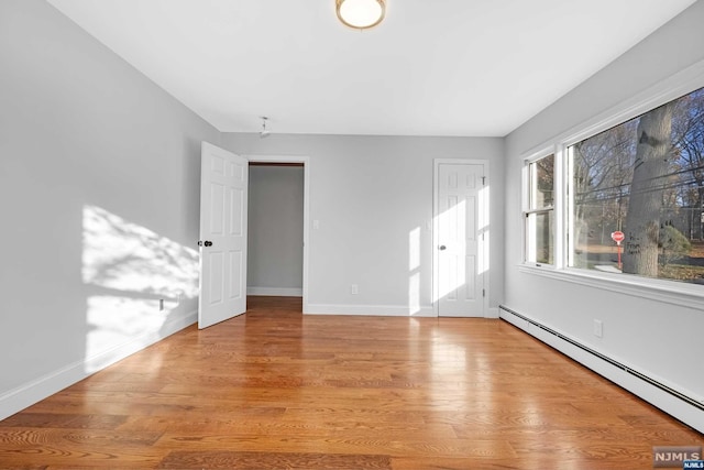 empty room with light wood-type flooring and a baseboard heating unit