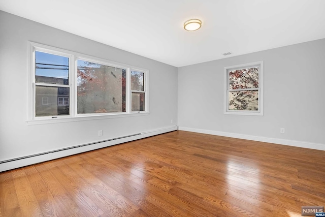 empty room featuring wood-type flooring and a baseboard heating unit