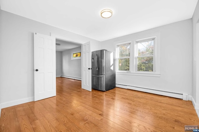 empty room featuring a baseboard radiator and light hardwood / wood-style flooring