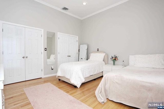 bedroom featuring wood-type flooring, two closets, and ornamental molding