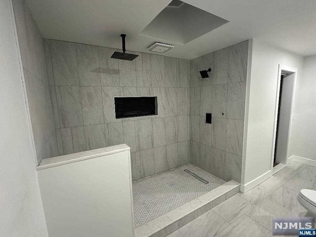 bathroom with a tile shower and toilet