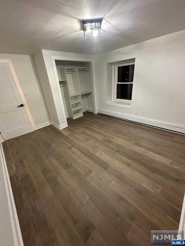 unfurnished bedroom featuring baseboard heating, a closet, and dark wood-type flooring