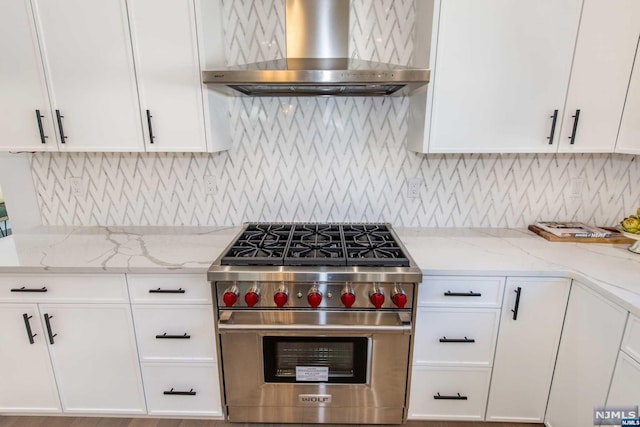 kitchen featuring white cabinets, luxury range, light stone countertops, and wall chimney range hood